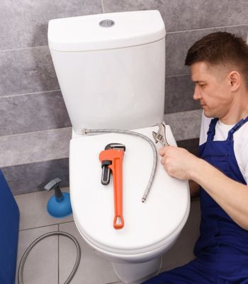 Professional Plumber Fixing Toilet Bowl in Restroom