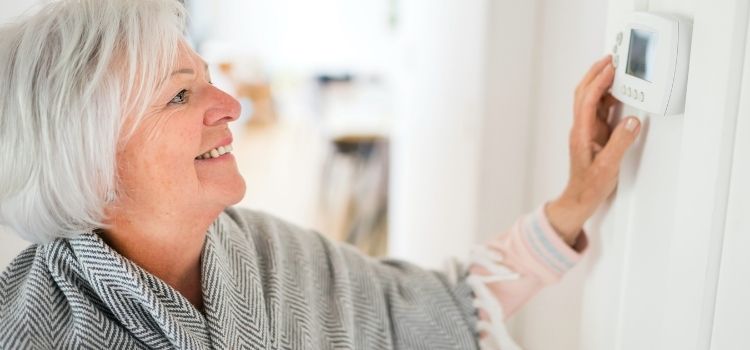 Senior woman adjusting her thermostat at home