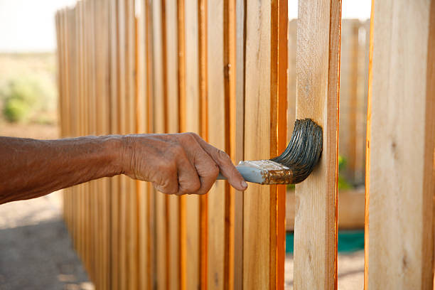 reliable fence handyman from Handyman Connection in Machesney Park, IL, applying stain to a wooden fence for a homeowner