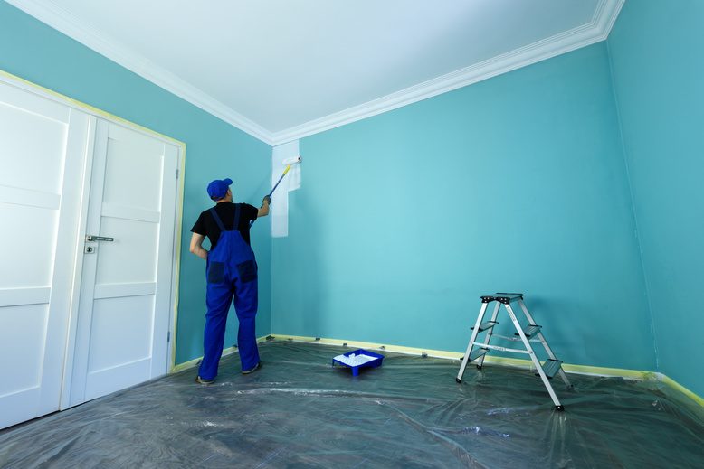 handyman using a roller brush to paint the interior of a home living room