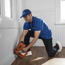 craftsman using nailgun to install baseboard moulding